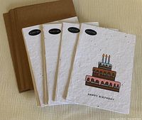 Photo of four seed paper birthday cards showing cake design with three candles and 'Happy Birthday' text, along with matching brown envelopes.