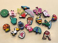 Photo showing 20 colorful shoe charms with various themes including animals, food, sports, and symbols.