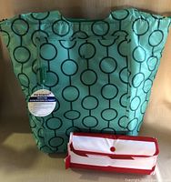 Large green insulated cooler bag with circular pattern, California Innovations brand label, and Microban antimicrobial protection tag alongside a folded smaller red and white cooler bag.
