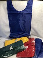 Front view of blue sports team pinnie with folded yellow, green, and red pinnies under it.