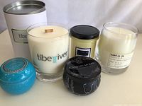Five new candles in various containers including glass jars and tins shown together on a white background.