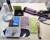 Photo of all lot items including pink wavy hair iron, sleep mask packaging, eyelash extensions, Dior pouch, cosmetic boxes, and other accessories on white surface