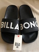 Top view of the pair of black slides, showing the Billabong brand name across the straps and attached tag.