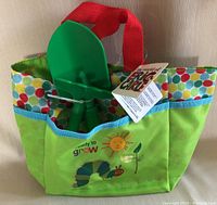 Colorful Eric Carle branded kids gardening bag with two green plastic gardening tools inside, shown fully assembled and new condition.