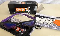 Ken Block Spy+ Helm sunglasses with blue mirrored lenses and purple-black frame shown with soft pouch and box.