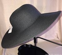 Side view of the black wide brim sun hat showing its shape and texture with attached tag.