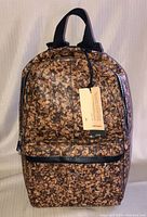 Front view of the backpack showing brown cork-like material with black zipper and handle.