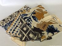 Set of four patterned tea towels folded and tied with fabric strap, showing a variety of blue, brown, ochre, and beige motifs.