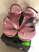 Front view of new pink women's sandals on top of their box showing velcro straps and footbed design.