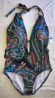 Single image showing the full one piece swimsuit laid flat, highlighting the halter neck tie, colorful paisley pattern, and deep V neckline.