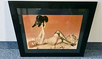 Full view of the framed pin-up art print, showing the woman lying on a tiger rug holding a black cat, with a black frame and mat.