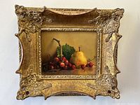 Frontal view of ornate gilt frame with still life painting of grapes and pear
