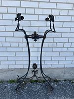 Full view of the wrought iron Art Nouveau stand showing three legs and three upward curving leaf figures on top.