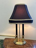 Front view of the Empire style twin column table lamp with black fabric shade on wooden surface indoors.