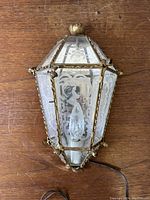 Full view of the antique etched glass wall sconce lying flat on a wooden surface, showing the detailed etched glass and metal frame with wiring extending from the bottom.