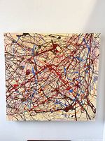 Front view of large abstract painting on canvas showing thick textured colorful drips and splatters in red, blue, black, and other colors on cream background.