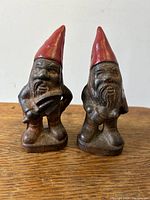 Front view of pair of vintage cast-iron gnome door stops, showing red hats, bearded faces, and stance with hands on hips.