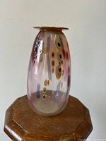 Frontal view of iridescent pink art glass vase showing abstract oval and linear designs on curved body, gold-toned lip visible at mouth.