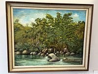 Front view of framed oil painting showing detailed riverbank with trees and rocks.
