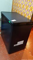 Black chest freezer from angled side showing the overall shape and condition.