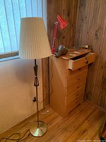 Wide view photo showing MCM floor lamp standing on the floor with two adjustable desk lamps on nearby furniture. Floor lamp has metal and teak base with pleated fabric shade.