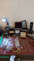 Overview photo showing wood jewelry boxes, plastic bags of jewelry, chain necklaces, and other accessories on table.