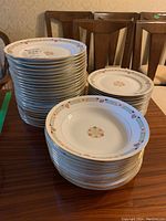Stacks of plates and bowls showing floral pattern and gold trim, demonstrating lot contents.