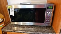 Front view of Panasonic microwave on countertop showing stainless steel and black glass door with MaxSold sticker.