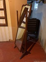 Full view of the vintage full-length mirror on its wooden stand in a basement setting.