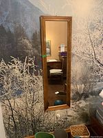 Full view of the wood framed wall mirror hanging against a nature-themed wallpaper background.