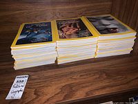 Three stacks of National Geographic magazines on a wooden shelf with yellow-bordered covers visible.