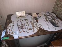 Overview of the collection laid out on a wooden table with white placemats, showing multiple necklaces, bracelets, and pins in a box.