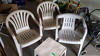 Photo showing three beige plastic patio chairs arranged around a small square plastic table in a garage or storage area