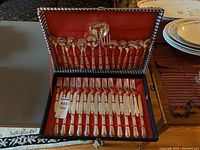 Open case showing the incomplete silver plated cutlery set with spoons and knives arranged in red fabric lining.