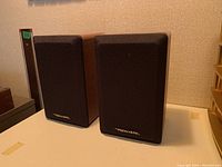 Pair of Realistic speakers with black grilles, wood tone sides, placed on a white surface.