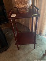 Wooden stand with one shelf placed near window and curtains. Turned legs and dark wood finish visible.