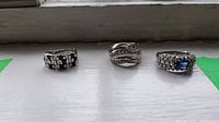 Three sterling silver rings arranged on a white surface by a window, showing overall view of all rings