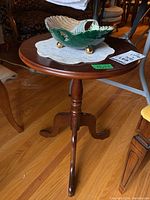 Side view of the round stained wood side table showing the turned pedestal and three curved feet