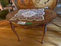 Top angled view of antique oval table with floral inlay, brass accents, and lace doily.