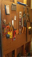 Hand tools hanging on pegboard including hammers, wrenches, crowbars, caulking gun, a level, and various small tools and hardware items.