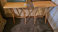 Two wooden folding TV tables side by side against a wall with vintage wallpaper.