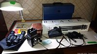 Full lot including Blacks BX45 tripod in box, Lubitel twin lens reflex camera, Vivitar 35EF camera, Jason 7x34 binoculars, steel binder clips, lamp, and mirror on table.