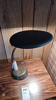 Photo of the vintage metal desk lamp showing its profile with oval black shade and metal base on a wooden surface.