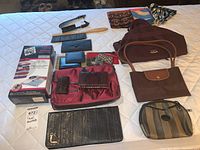 Photo showing all items including wallets of various styles, two brushes, two scarves, purses, and the Space Bag storage pack box arranged on a bed.
