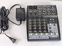 Top view of Behringer Xenyx 802 mixer with connected power adapter showing control knobs, input/output ports.