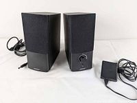 Two black Bose speakers and power adapter shown from front