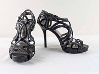 Pair of black Calvin Klein high heel sandals with multiple straps, buckle closure, and stiletto heels shown side by side.
