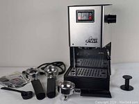 Front view of Gaggia Classic machine on white surface with accessories laid out