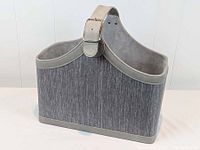 Grey rectangular storage basket with vegan leather trim and fabric body shown from front angle on white surface and white wall background.