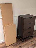 Unassembled IKEA TRYSIL 4-drawer chest in two unopened boxes displayed next to an assembled chest for reference only, which is not included.